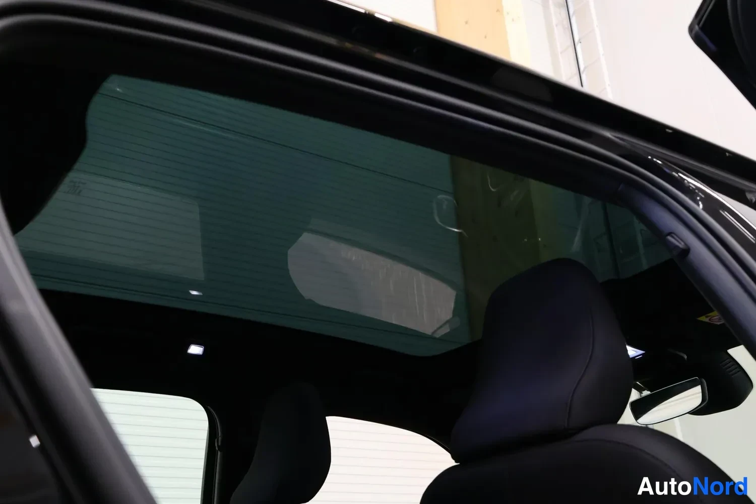 Yksityiskohta: Sisätilan näkymä panoraamalasikaton alle oikean etuistuimen pääntuen takaa, katossa peili ja tumma verhoilu.