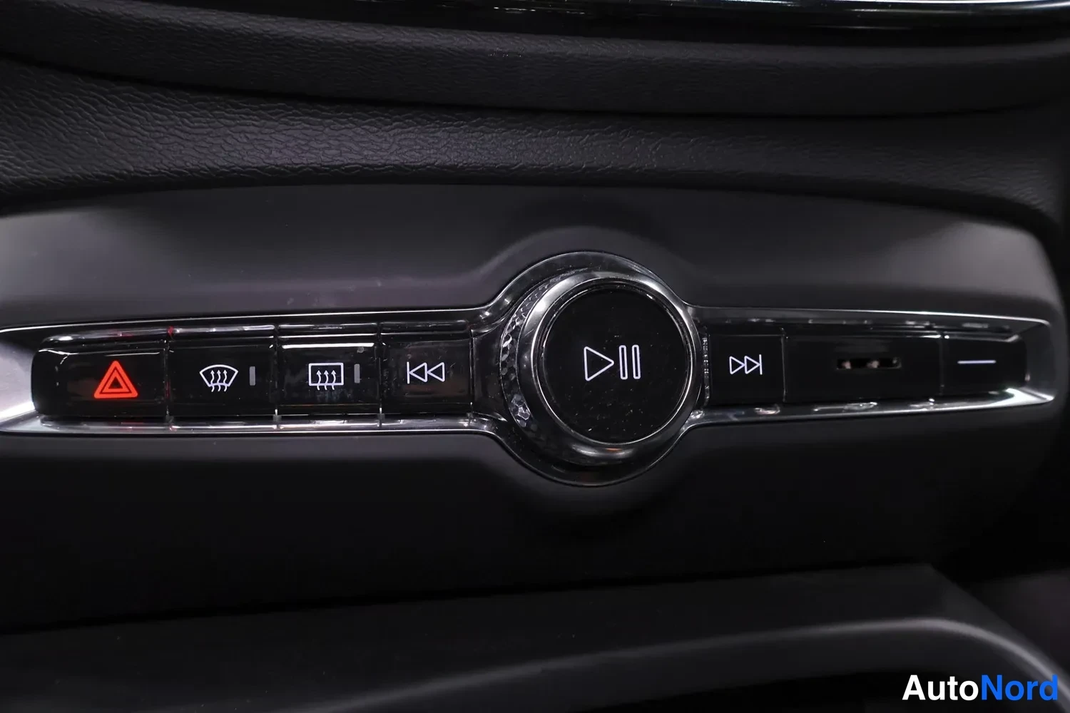 Yksityiskohta: Detail of dashboard controls including illuminated red hazard light button, heated front windscreen icon, media playback button with pause symbol, USB ports, an