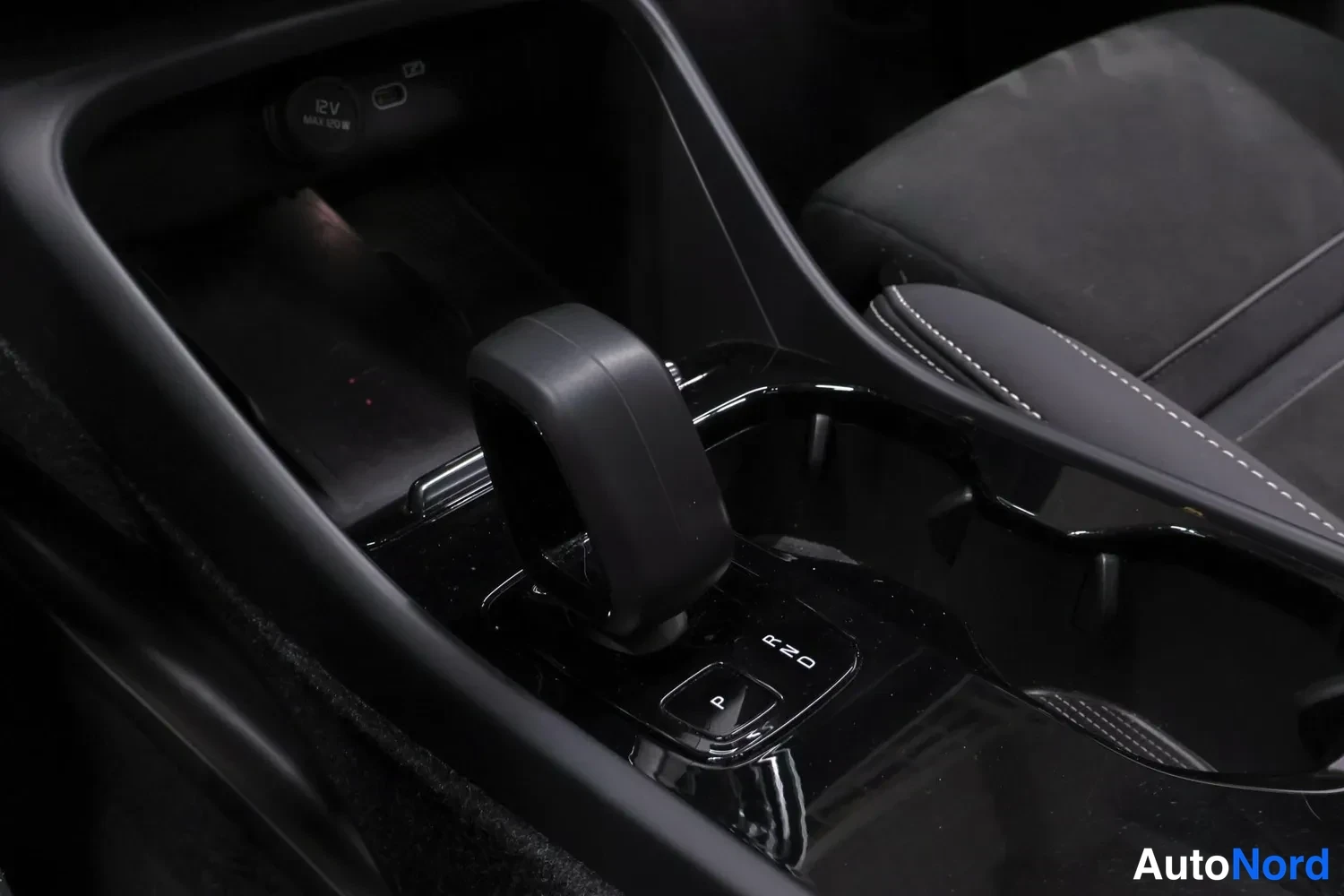 Yksityiskohta: Close-up view of center console featuring a small black gear selector lever, electronic parking brake switch labeled 'P', open storage compartment containing a