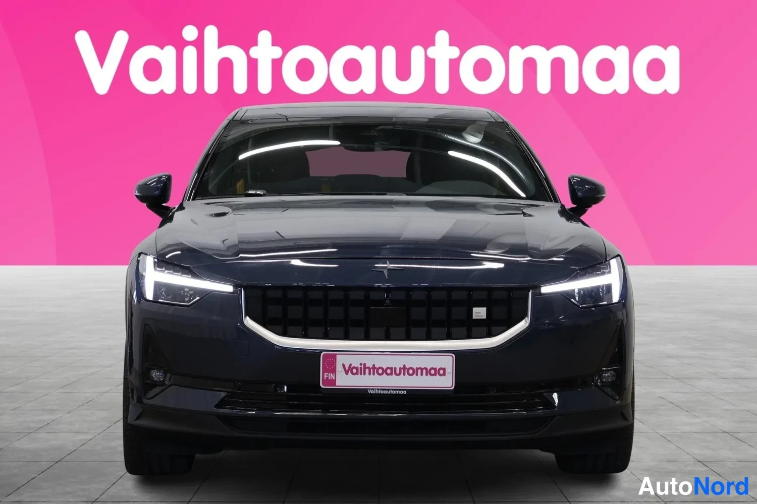 Edestä: Polestar 2 suoraan edestä kuvattuna; näkyvät ohutlinjaiset ajovalot, musta kori­säleikkö ja Vaihtoautomaaa-kilpien kehys.