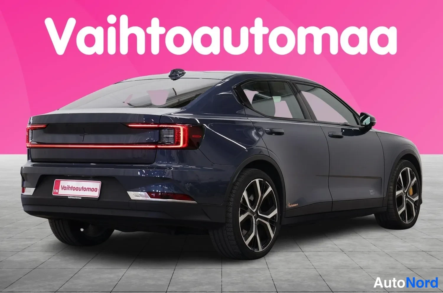Takaviisto: Auto kuvattu takaa viistosti vasemmalta, tummansininen sedan, takavalojennauhe ja vaihtoautomaa-kyltti näkyvät, kevytmetallivanteet mustat.