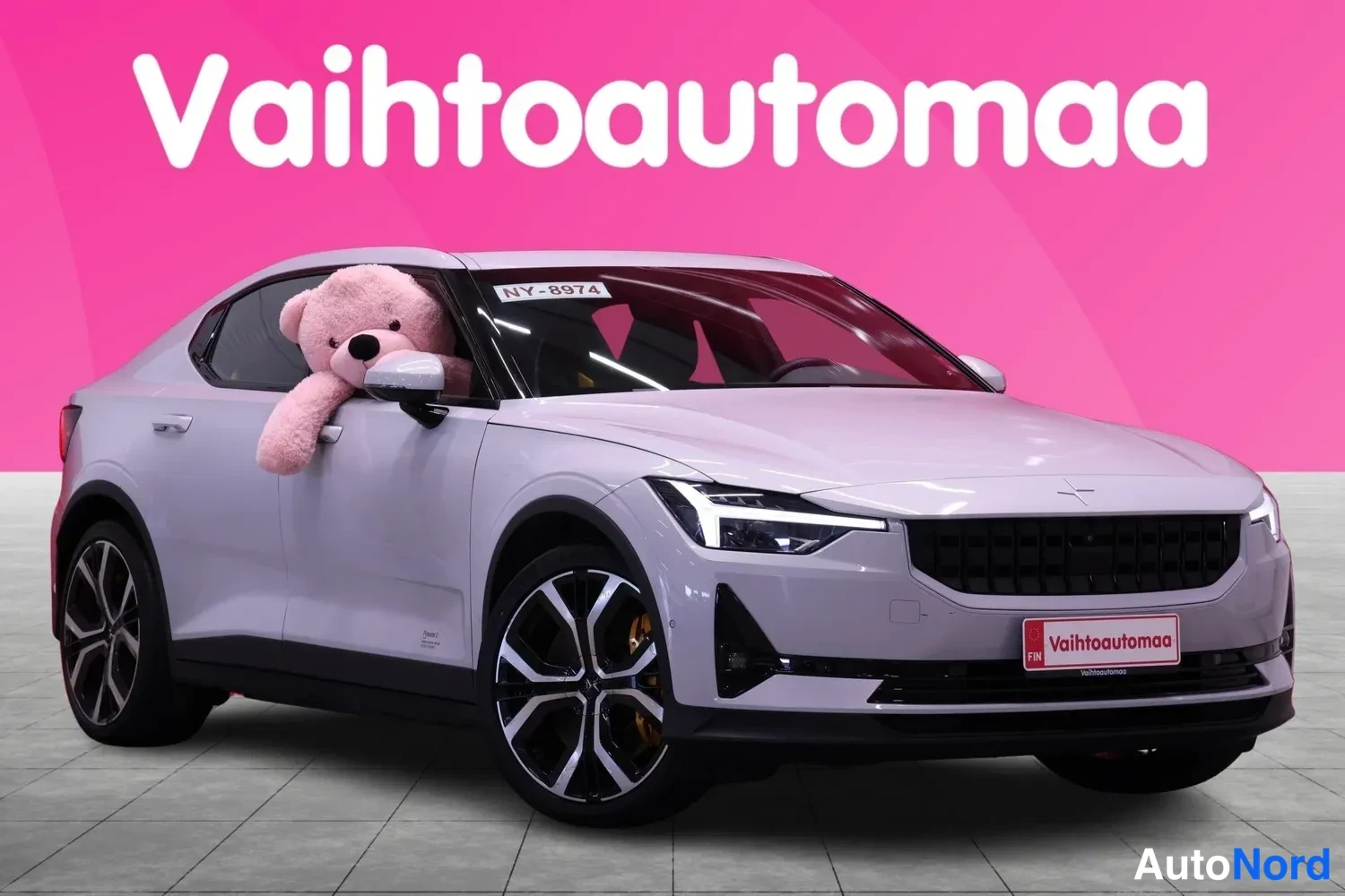 Etuviisto, nokka oikealle: Valkoinen Polestar 2 -sedan kulmasta edestä oikealta kuvattuna, pinkki Vahtoautomaa-tausta.