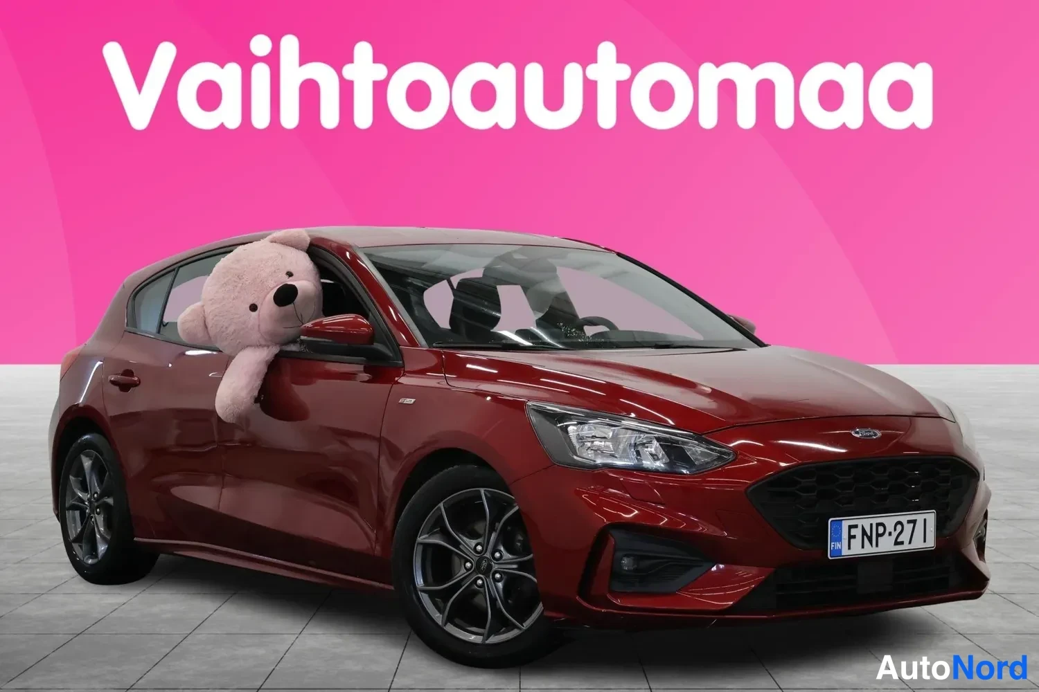 Etuviisto, nokka oikealle: Punaisenruskea Ford Focus -henkilöauto vinosti edestä oikealta kuvattuna, rekisteritunnus, pehmolelu takapenkissä ikkunassa.