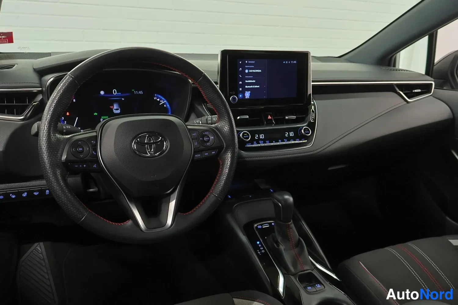 Edestä: Toyota-ohjauspyörä, digitaalinen mittaristo, keskikonsolin kosketusnäyttö ja automaattivaihteen valitsin.