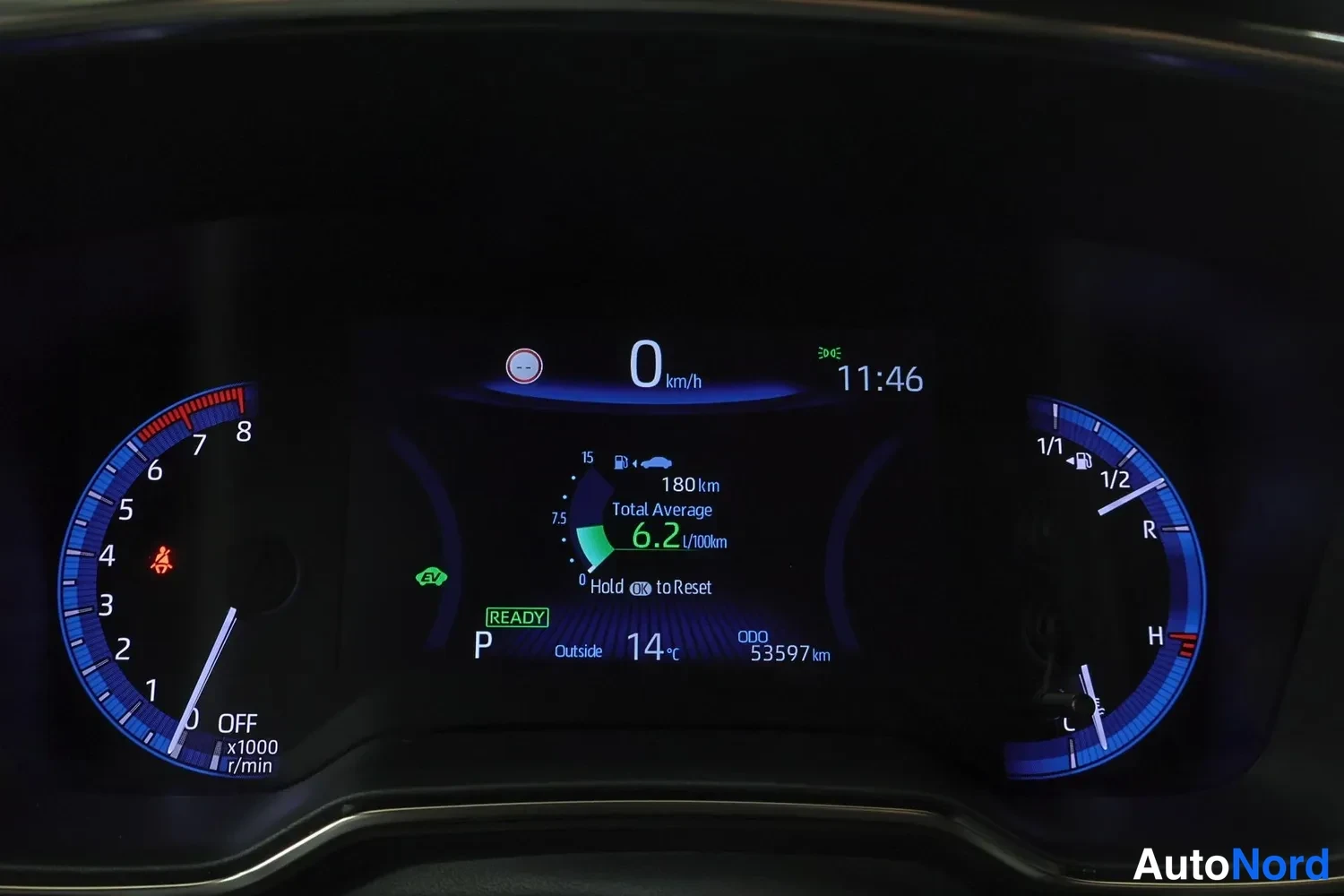 Yksityiskohta: Kojelaudan näyttö: nopeus 0 km/h, kellonaika 11:46, kokonaiskeskulukema 6,2 l/100km, OD0 53597 km, ulkolämpötila 14 °C ja READY-merkintä.