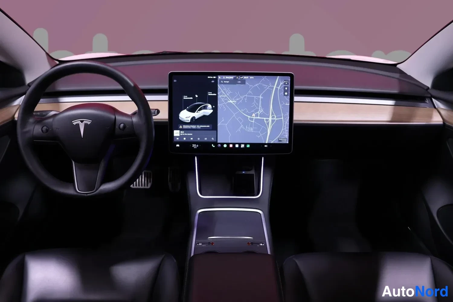 Edestä: Tesla-ohjaamon näkymä: ohjauspyörä, keskiruutu ja kartta näytöllä.