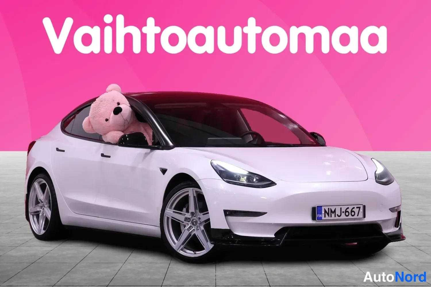 Etuviisto, nokka oikealle: Valkoinen Tesla Model 3 -henkilöauto edestä oikealta vasemmalle kuvattuna, rekisteritunnus.