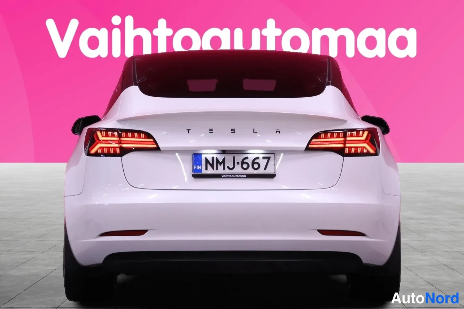 Takaa: Valkoinen Tesla Model 3 -henkilöauto suoraan takaa kuvattuna, rekisteritunnus.