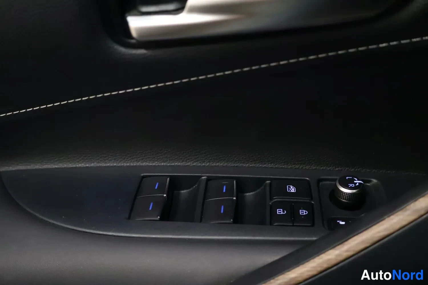 Ohjaamo: Driver-side door panel window controls: four switches with blue backlighting for power windows, two lock switches, and a circular mirror adjustment knob to the