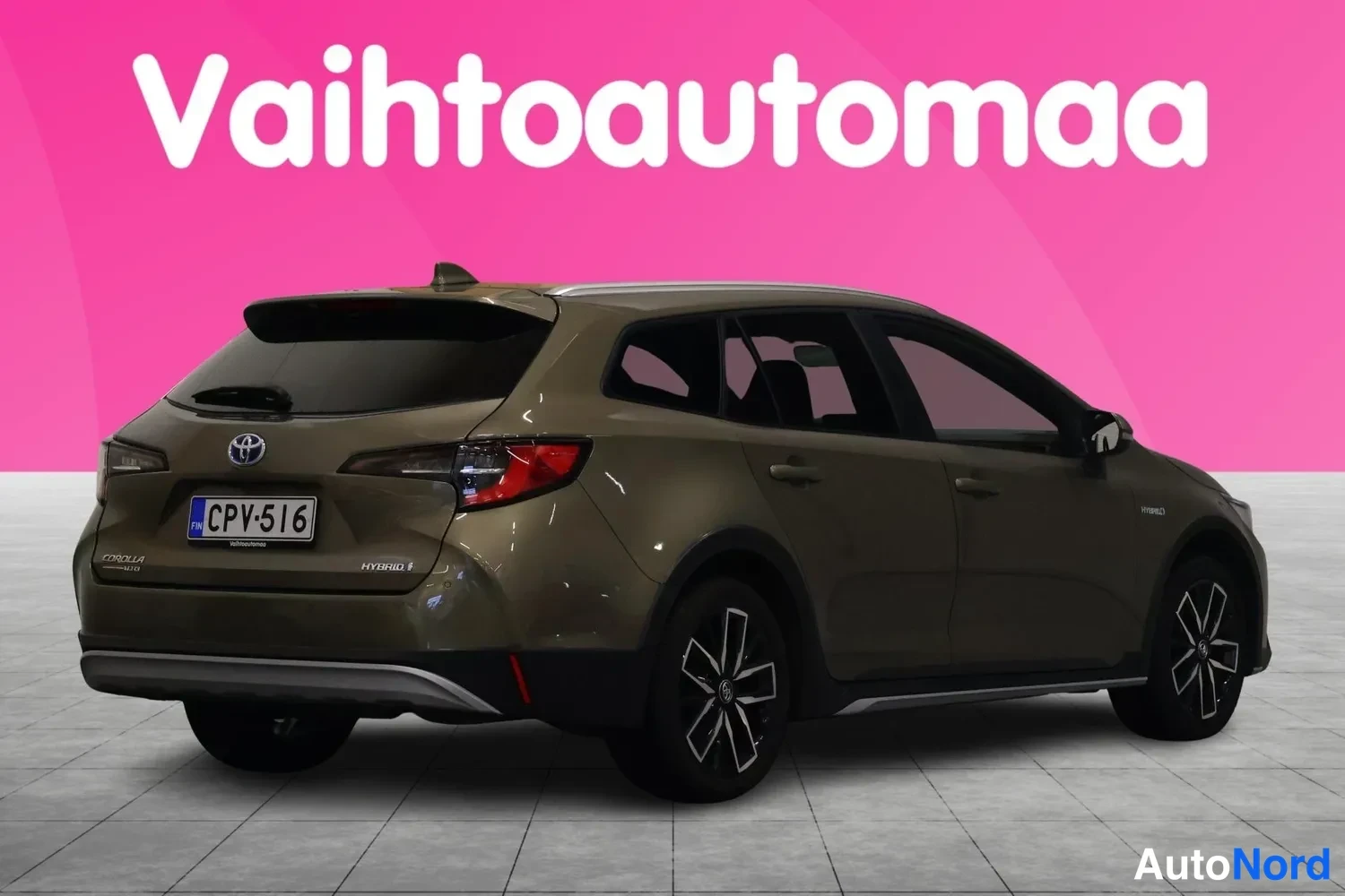 Takaviisto: Takaviistokuva ruskeanvihreästä farmariautosta: rekisterikilpi, HYBRID-tunnus takaluukussa, takaspoileri ja kevytmetallivanteet; taustassa pinkki Vaihtoautoma-b