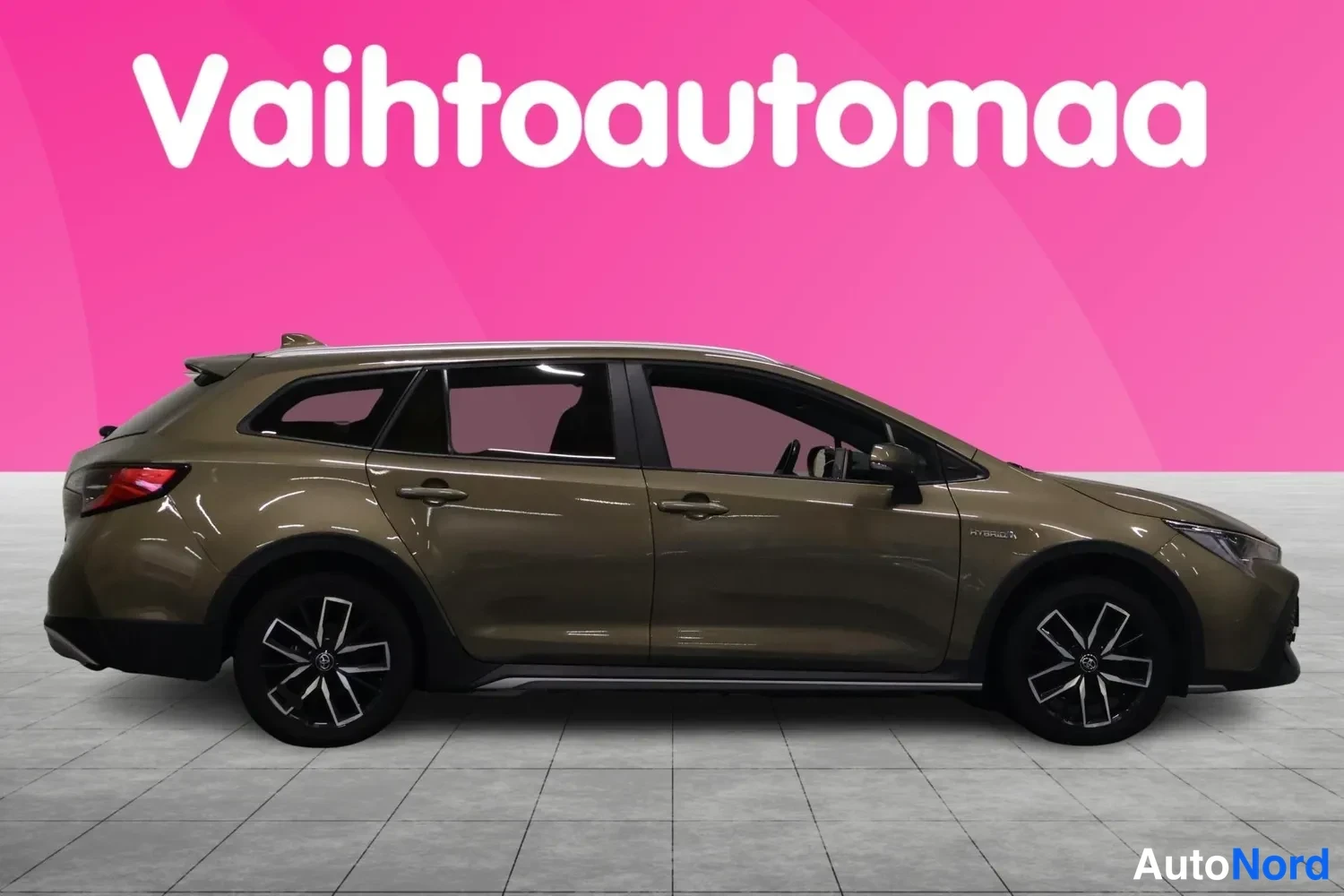 Sivulta: Vaihtoautomaa-taustalla ruskean farmariauto sivusta, vasen kylki ja kolme pyörää näkyvissä.