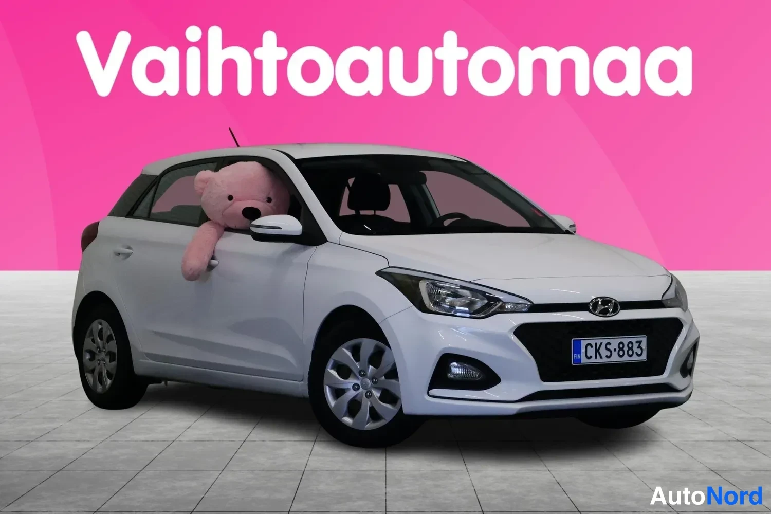 Etuviisto, nokka oikealle: Valkoinen Hyundai-nakunen henkilöauto kolmivartalokuva edestä oikealta, rekisteri, pinkki tausta ja Vahtoautomaa-logo.