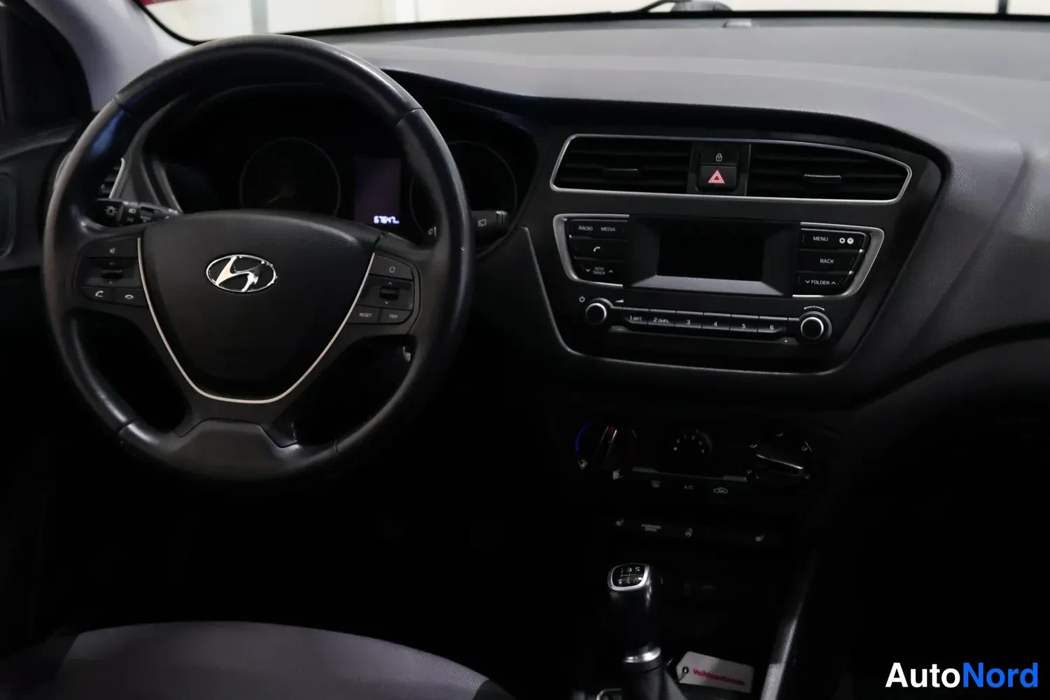 Muu: Ohjaamon yleiskuva: ohjauspyörä ja Hyundai-merkki, kojelauta sekä keskikonsoli manuaalivaihteen vivulla.
