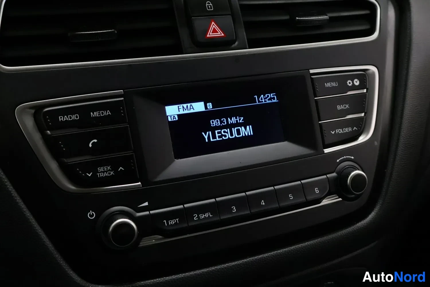 Muu: Keskikonsolin radiopaneeli lähikuva: näytössä FMA 99.3 MHz YLESUOMI ja kello 14:25, napit RADIO, MEDIA, MENU, BACK.
