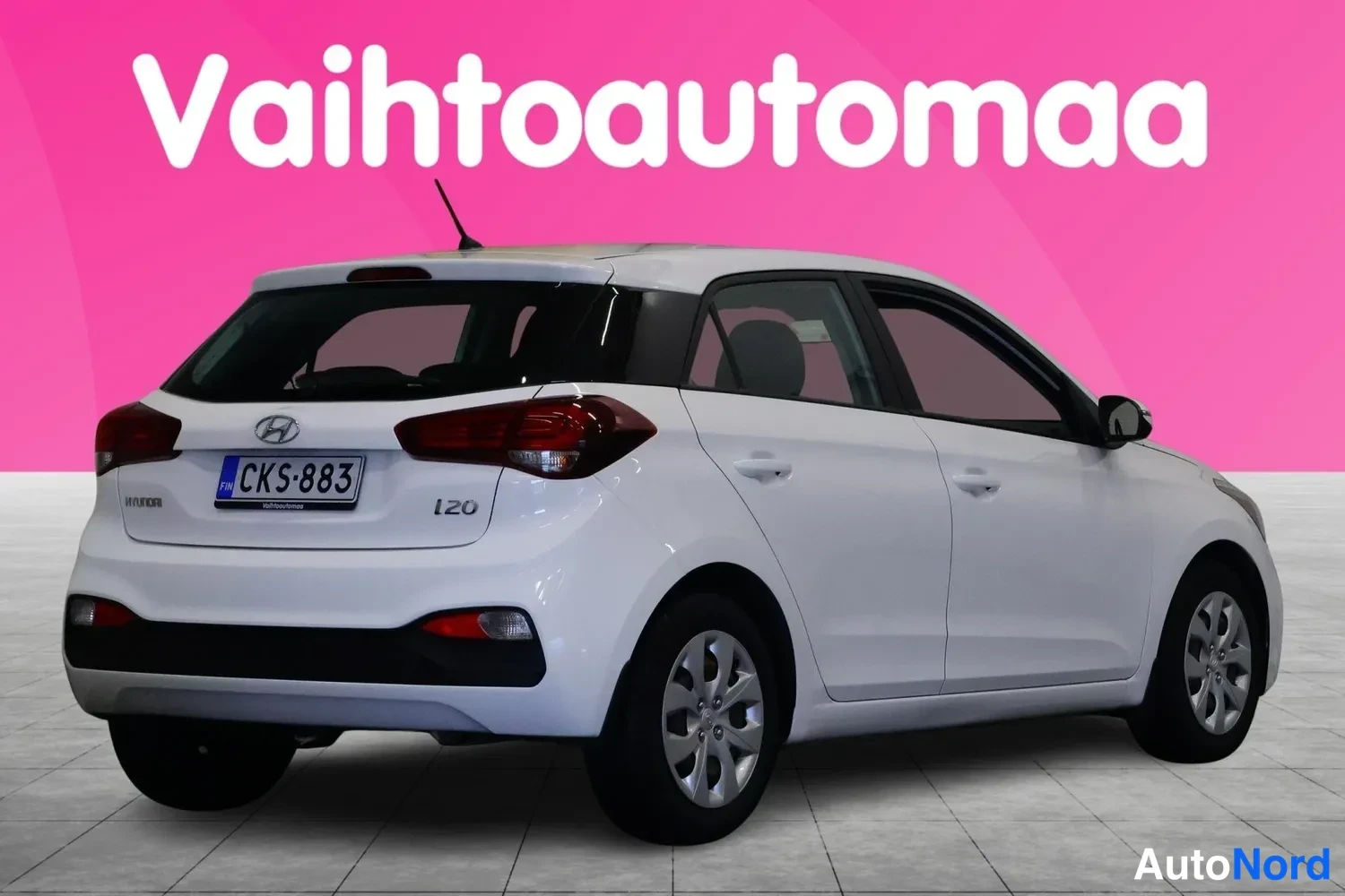 Takaviisto: Hyundai i20 -viistä takakulmaa valkoinen vetoauto, rekisterikilpi, pinkki tausta.