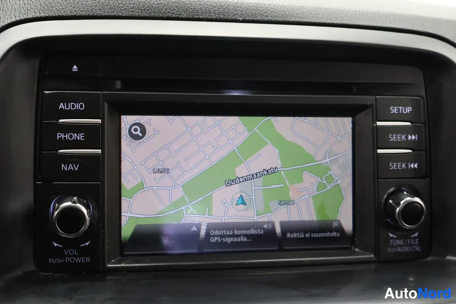 Yksityiskohta: Kojelautaan integroitu infotainment-näyttö näyttää karttaan perustuvan navigaattorin, jonka viestissä lukee 'Odottaa kunnollista GPS-signaalia...'.