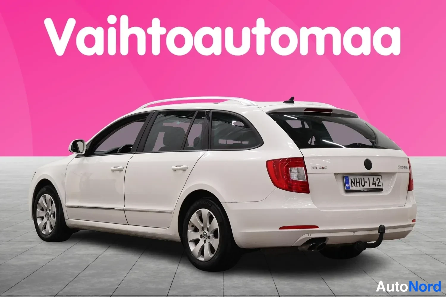 Takaviisto: Auton takakulma vasemmalta: valkoinen farmariauto, kylki ja takamootti näkyvät, rekisteritunnus, kattokaiteet ja vetokoukku.