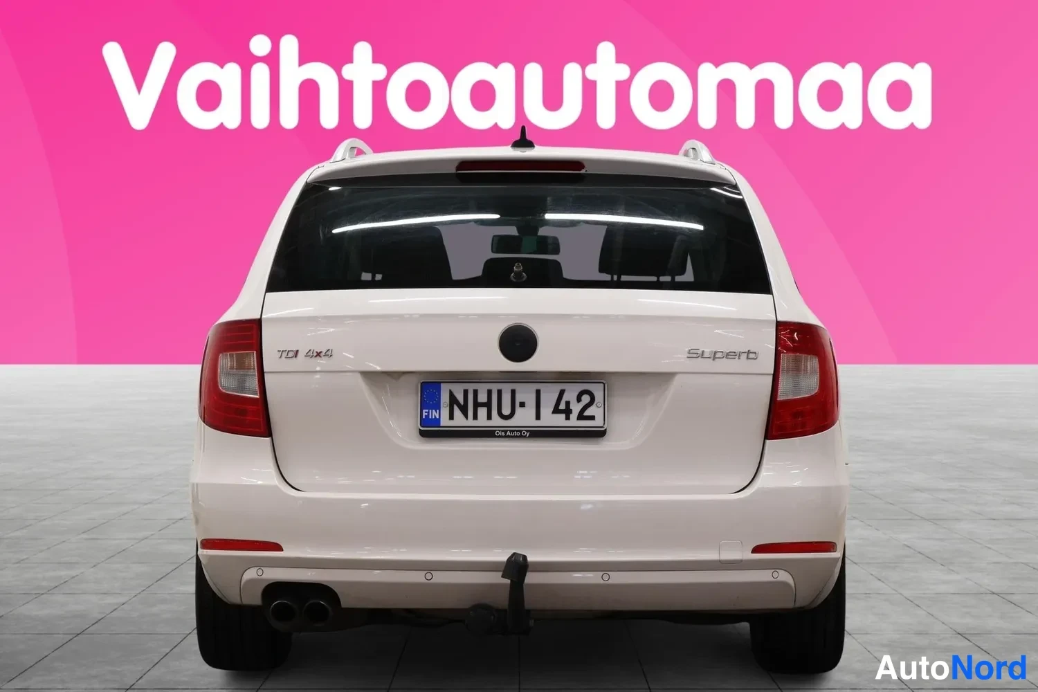Takaa: Auton takaosa suoraan takaa: valkoinen farmari, takavalot ja takaluukku näkyvät, rekisteritunnus, kattokaiteet.