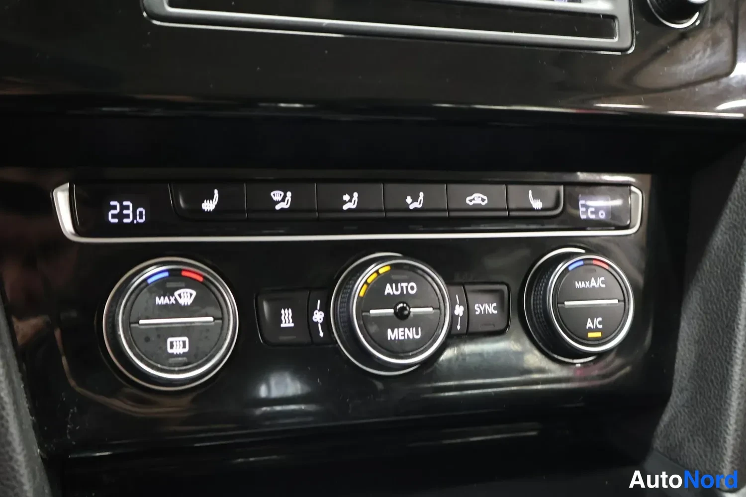 Muu: Avtomaatin ilmastointipaneeli, jossa lukee AUTO, MENU, SYNC, MAX A/C ja A/C, lämpötila 23.0, keskikonsolin musta pinta.