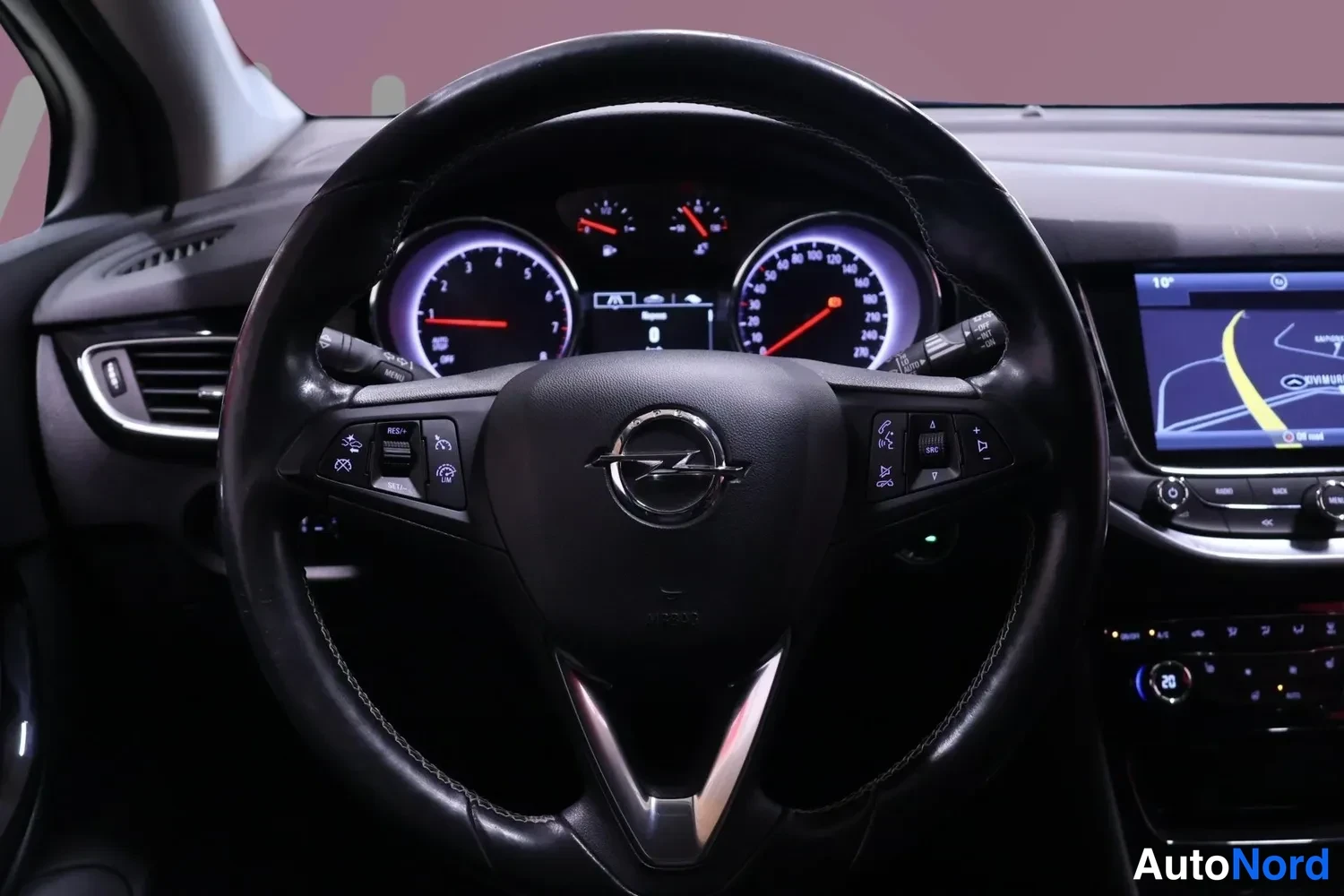 Muu: Ohjauspyörän lähikuva: Opel-logo, mittaristo ja ohjauspyörän puhesäätimet näkyvissä.