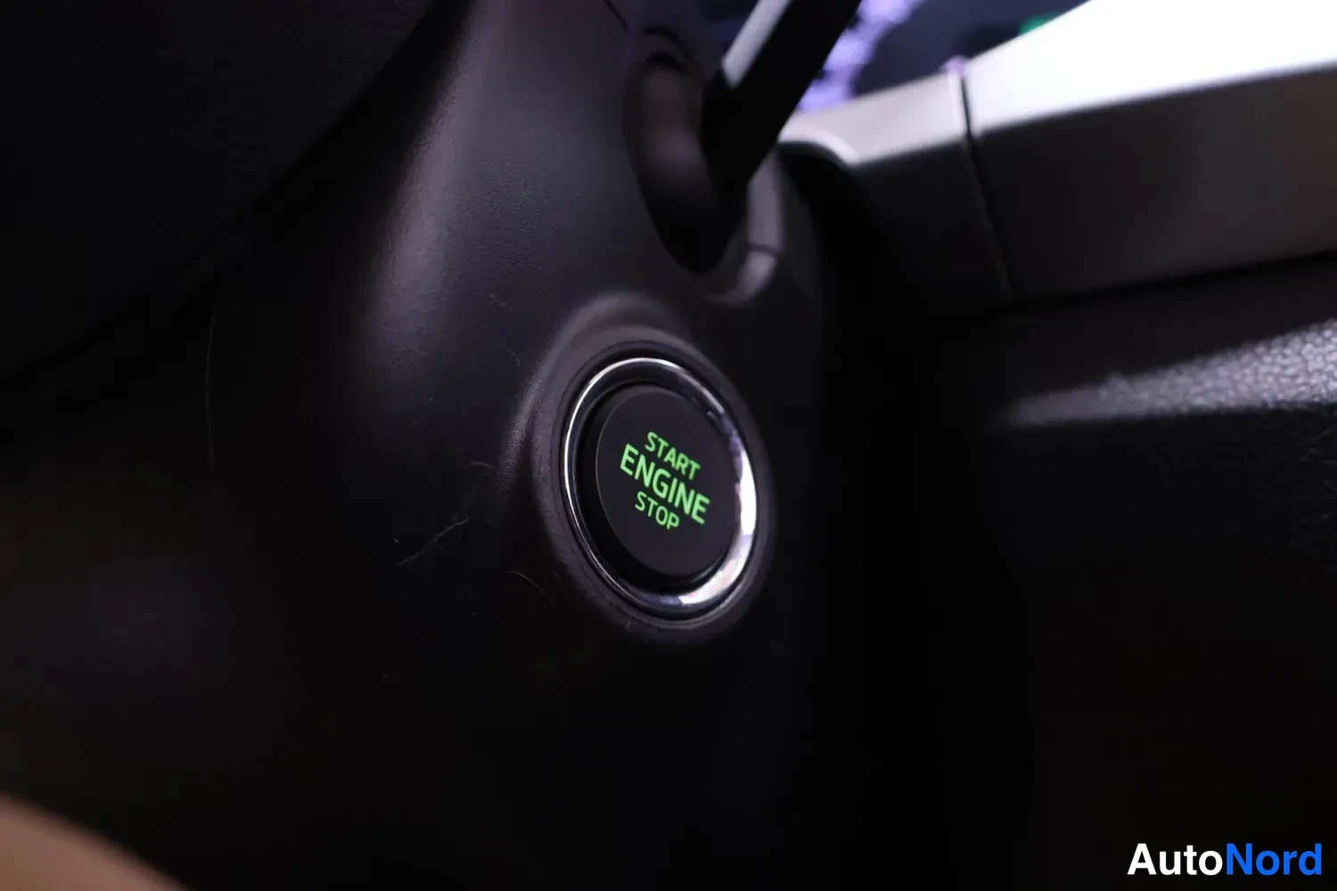 Muu: Starttipainike lähikuvassa kojelaudan vasemmalla puolella, vihreällä tekstillä START ENGINE STOP.
