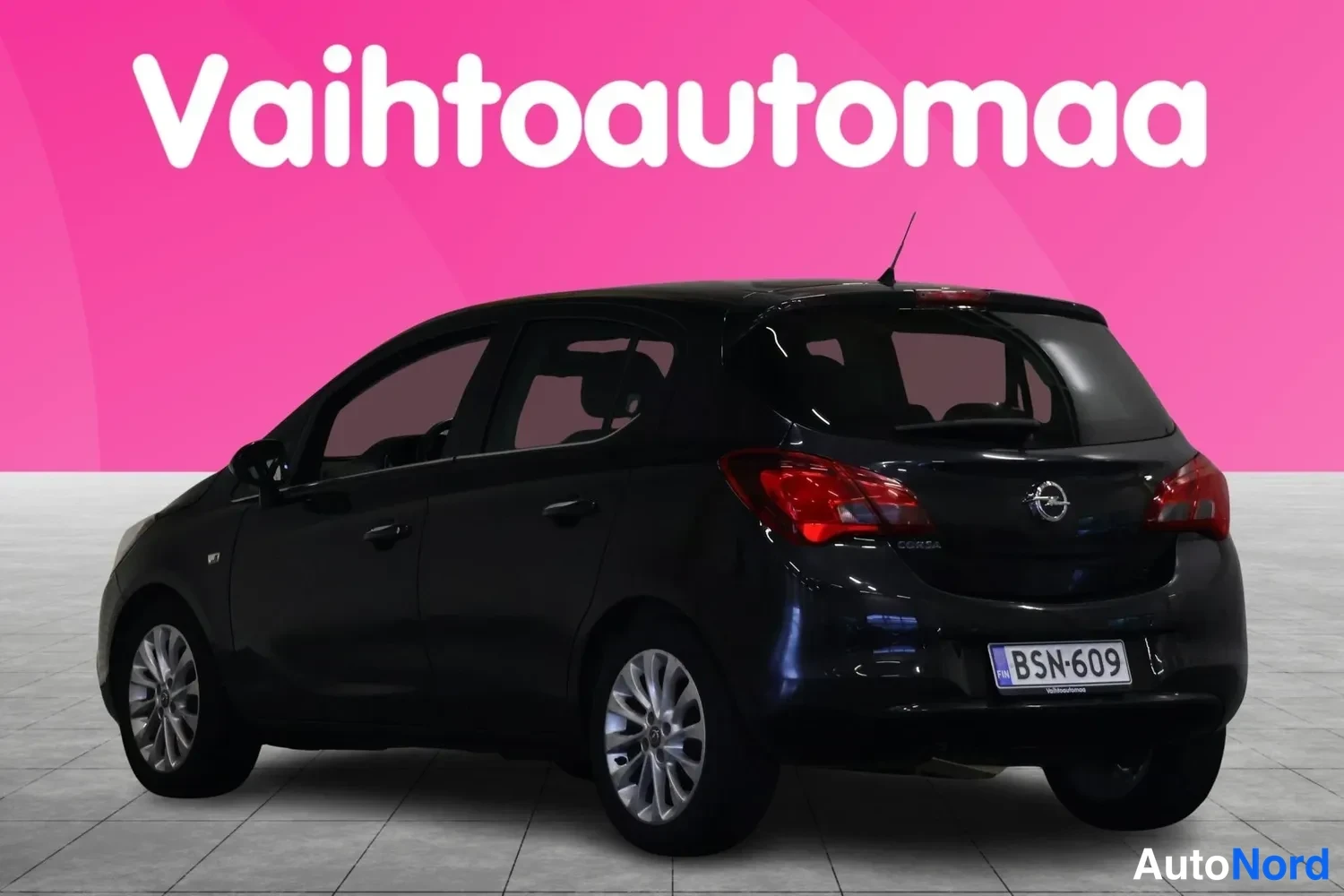 Takaviisto: Mustan hatchbackin takakulmakuva vasemmalta puolelta, rekisterikilpi, pinkki tausta.