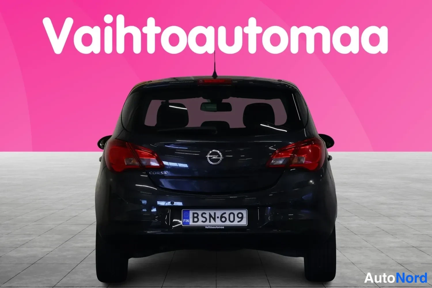 Takaa: Mustan hatchbackin suora takakuva, rekisterikilpi, korossa CORSA-teksti, pinkki tausta.