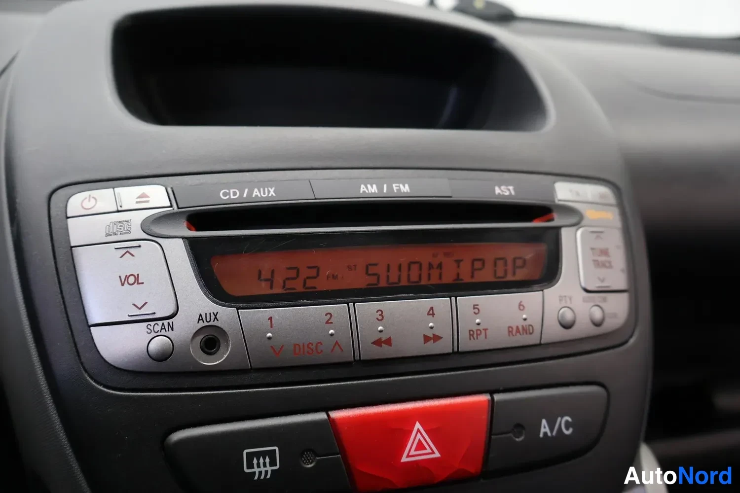 Muu: Kojeiston keskuskonsolin lähikuva: radio-CD-soitin, jonka näytössä lukee '422 FM SUOMIPOP', sekä A/C-nappi ja varoitusvalojen nappi.