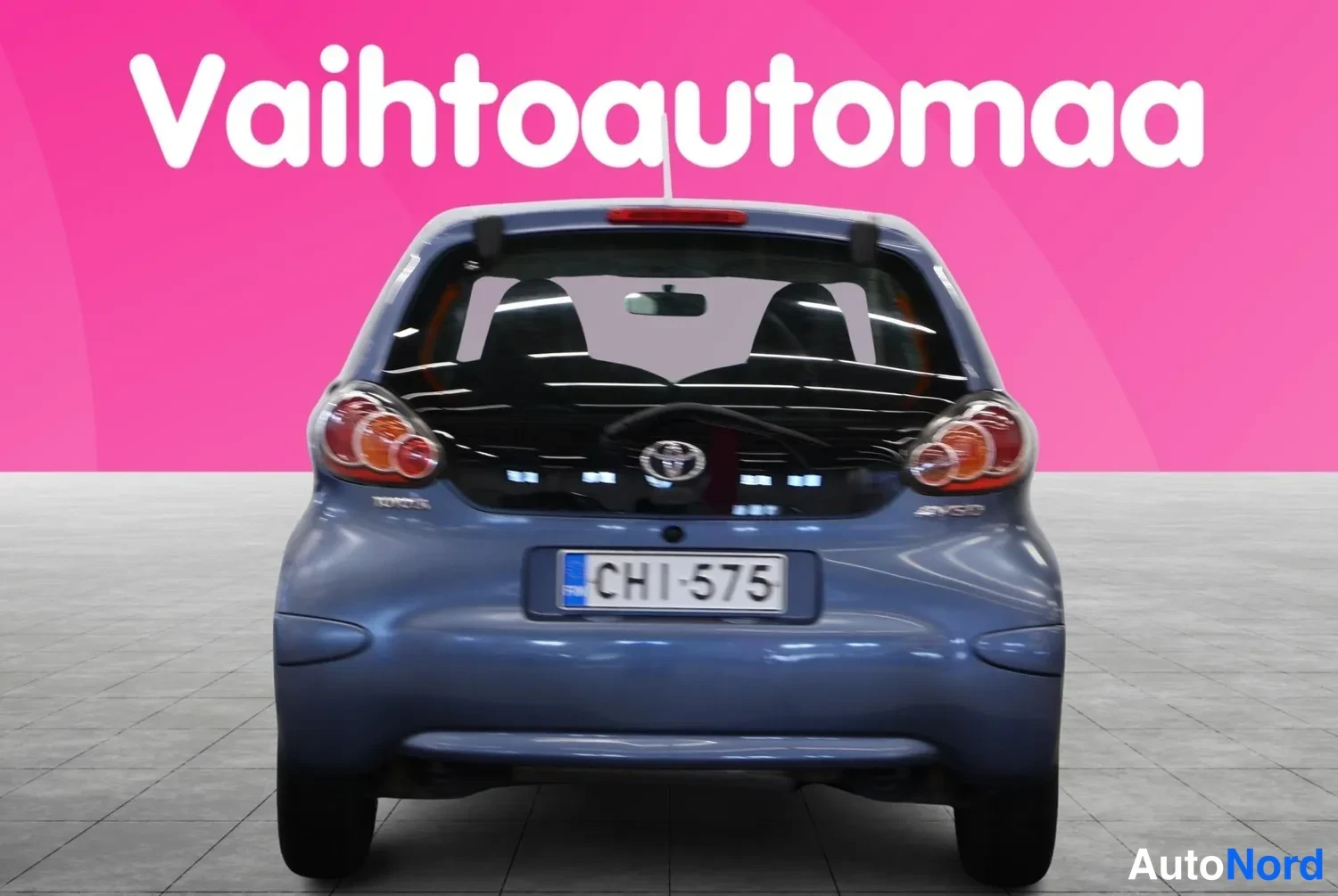 Takaa: Sininen Toyota Aygo suoraan takaa kuvattuna, rekisteritunnus, vaaleanharmaa studiovaaka.