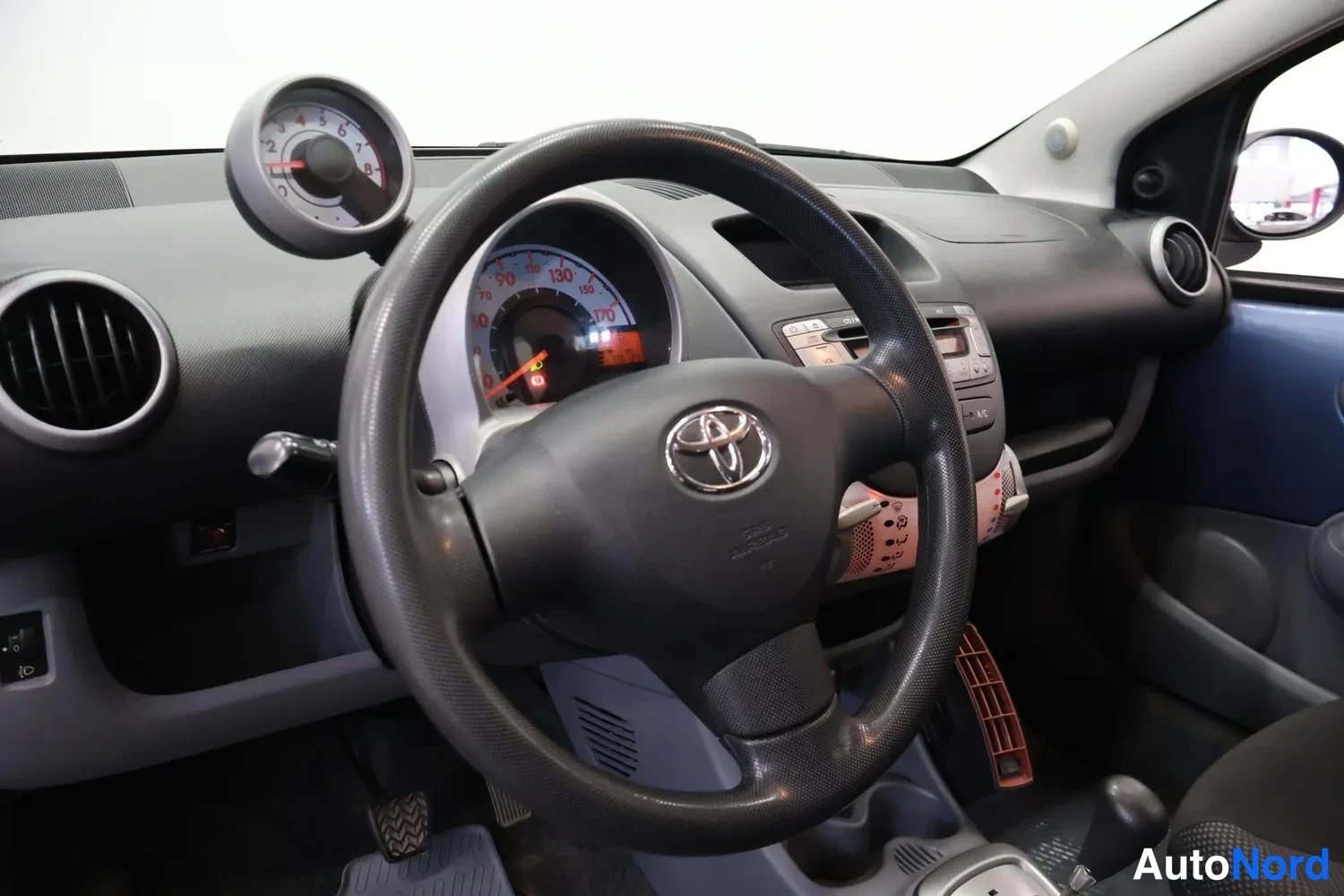 Muu: Kuljettajan näkymä Toyota-ohjauspyörästä: kojelaudassa nopeusmittari, erillinen kierrosmittari kiinnitettynä ylös ja keskiöconsolen radioyksikkö, voimansiirron
