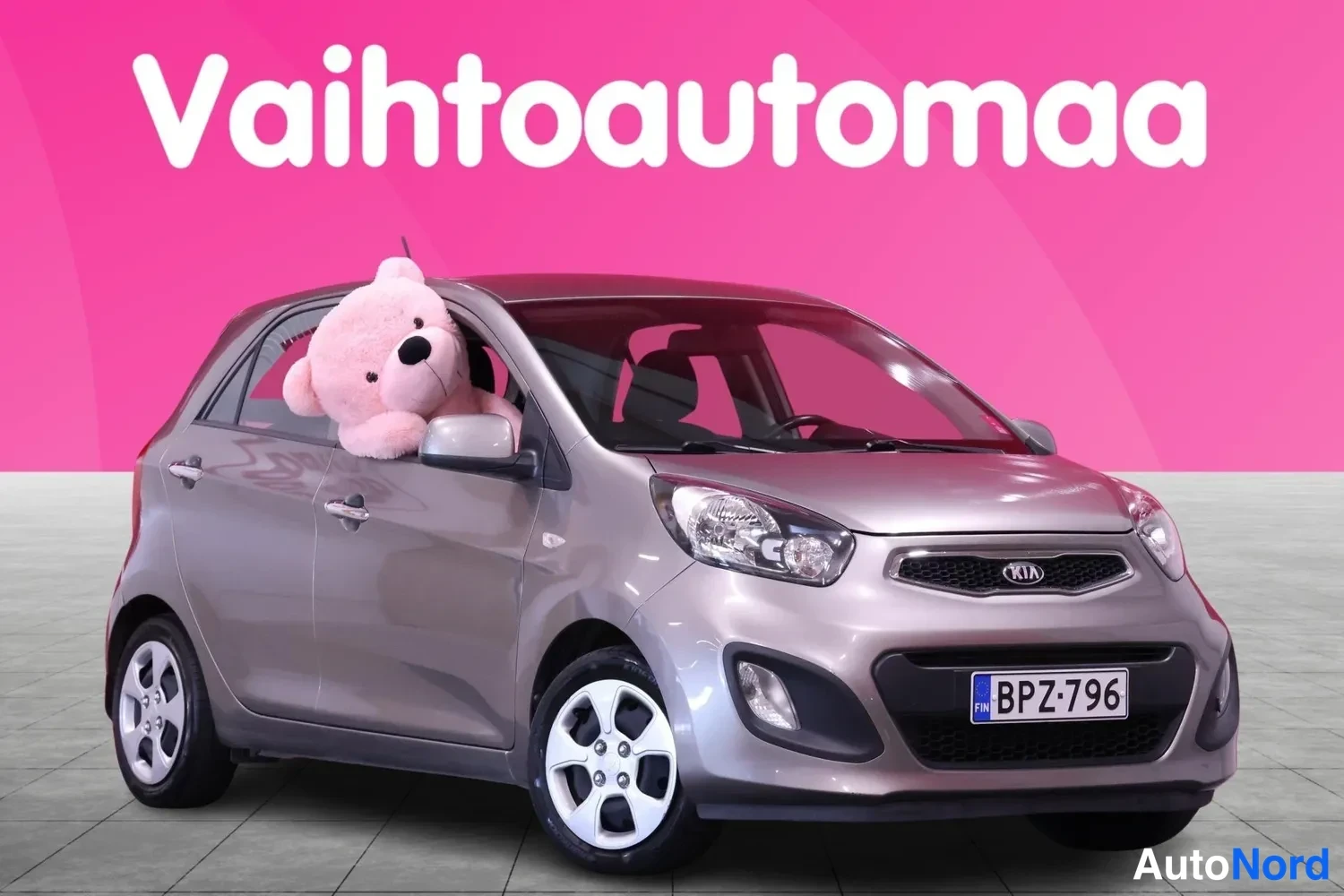Etuviisto, nokka oikealle: Kia Picanto -henkilöauto harmaassa etunurkkakuvassa rekisterillä, pehmolelu ikkunassa.