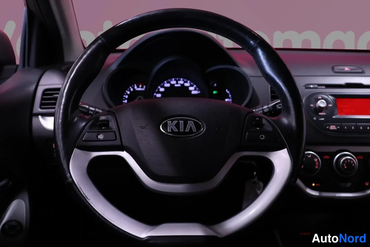 Muu: Ohjauspyörä KIA-merkillä, kojelauta ja radionäyttöAutojen sisätiloissa, tummassa valaistuksessa.