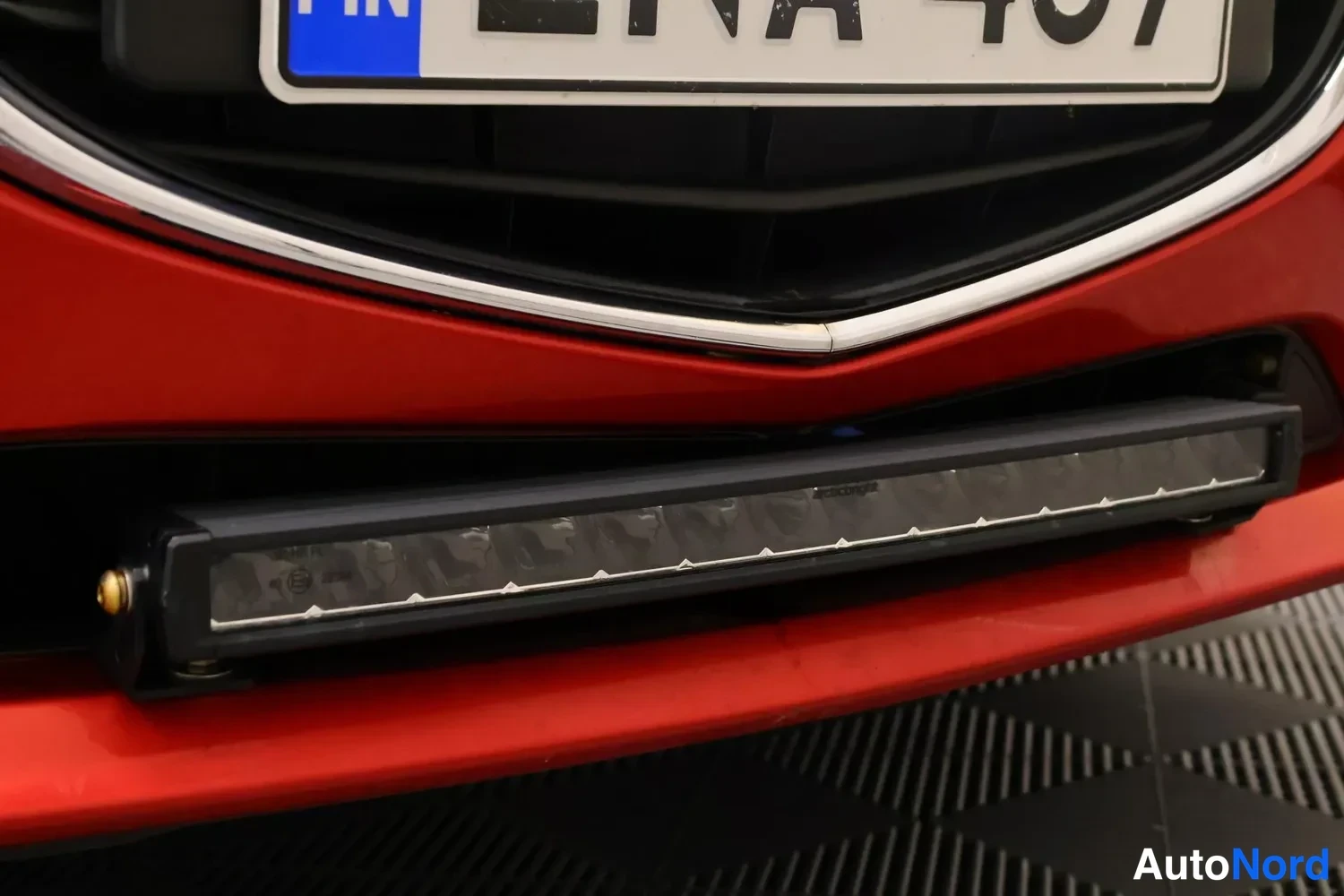 Edestä: Edullinen etusuuksi lähikuva punaisesta autosta. Etupuskurissa on ylimääräinen LED-kalustovalo. Etuvalaistus- ja puskurit osat ovat näkyvissä.
