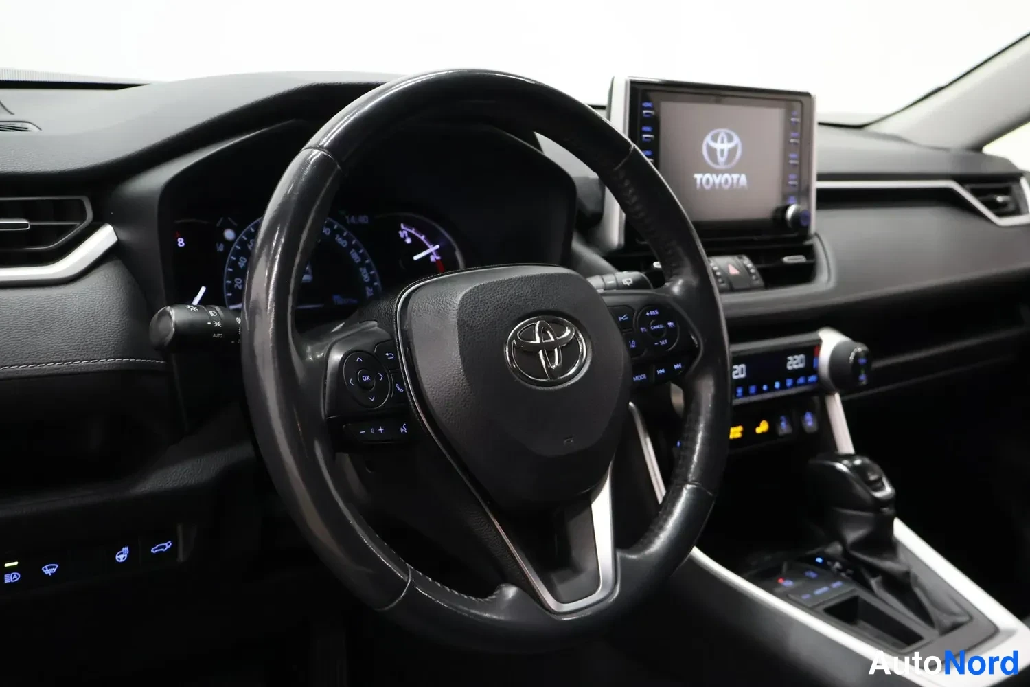 Muu: Ohjaamon sisäkuva: Toyota-merkkinen ohjauspyörä keskellä, kojelauta ja medianäyttö Toyota-logolla näkyvissä.