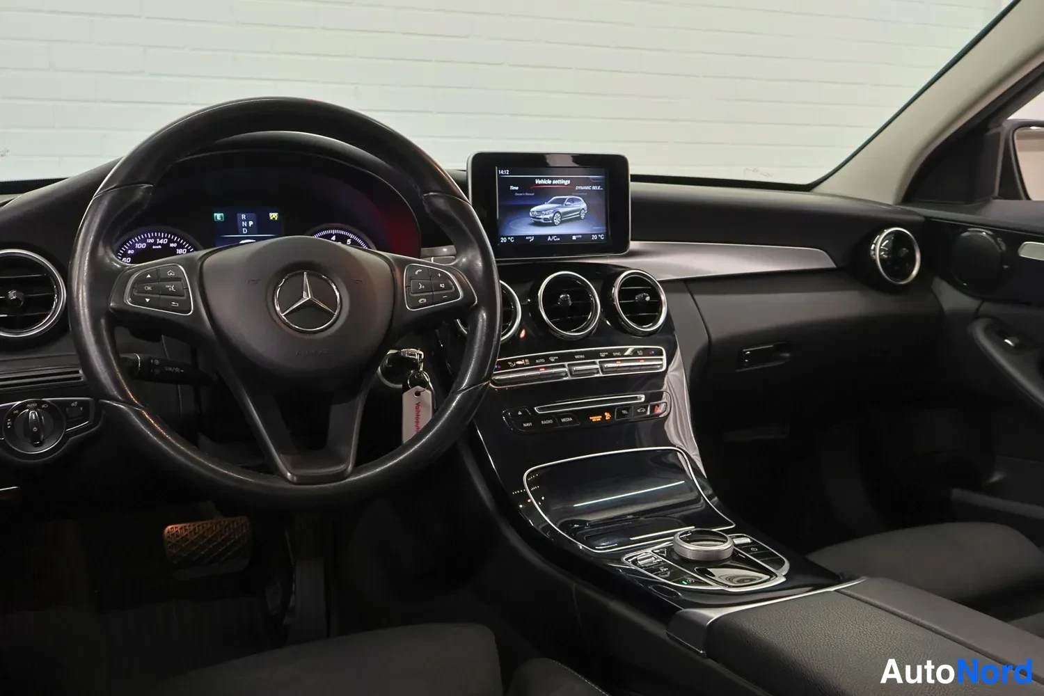 Edestä: Mercedes-Benzin ohjaamo kuljettajan puolelta: multitoimioratti, irtonäyttö jossa auto-kuva ja Vehicle settings -valikko, kolme pyöreää ilmastointiaukkoa, keskik