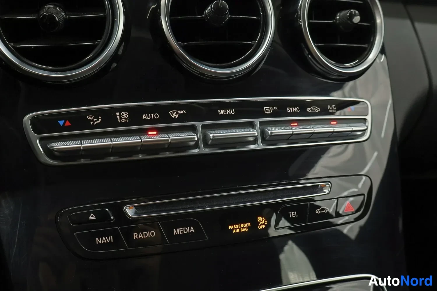 Muu: Sisäkuva kojelaudan ilmastointi- ja multimediapaneelista: kolme pyöreää ilmanvaihtoaukkoa, painikerivit AUTO, MAX, MENU, REAR, SYNC ja A/C REST sekä NAVI, RADIO