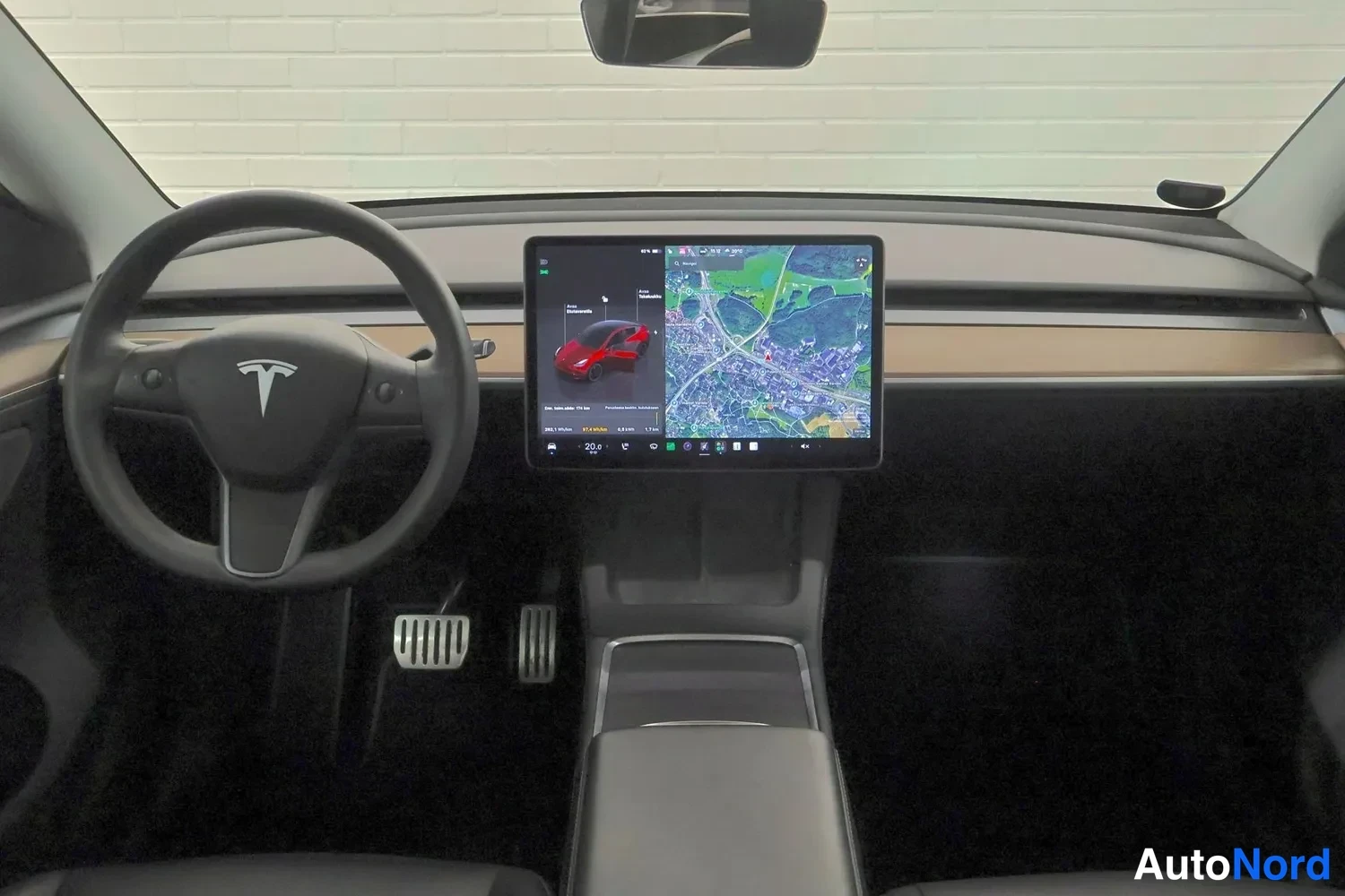 Muu: Tesla-autojen ohjaamo valosta eteenpäin kuvattuna: musta ohjaustvati Tesla-logolla, keskirivissä iso kosketusnayttö kartta- ja ajoneuvonäkymillä, puosävyinen ko