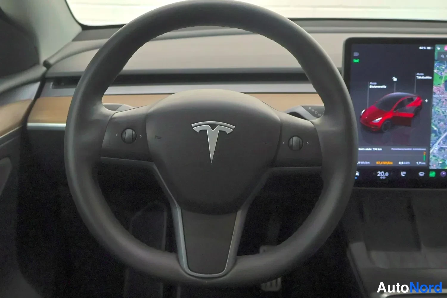 Muu: Tesla-autojen ohjauspyörä lähikuvassa; Tesla-logo keskellä ohjauspyörää ja suurempi kosketusnayttö taustalla näyttää ajoneuvon tilan.