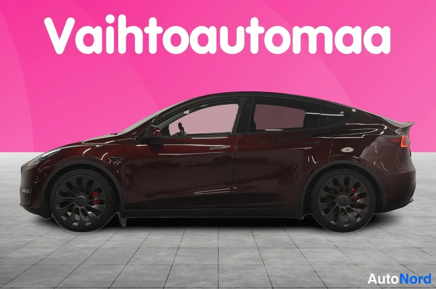Takaviisto: Tummansininpunaisen Tesla Model Y:n sivuprofiili, takavalo näkyy kuvan oikeassa reunassa.