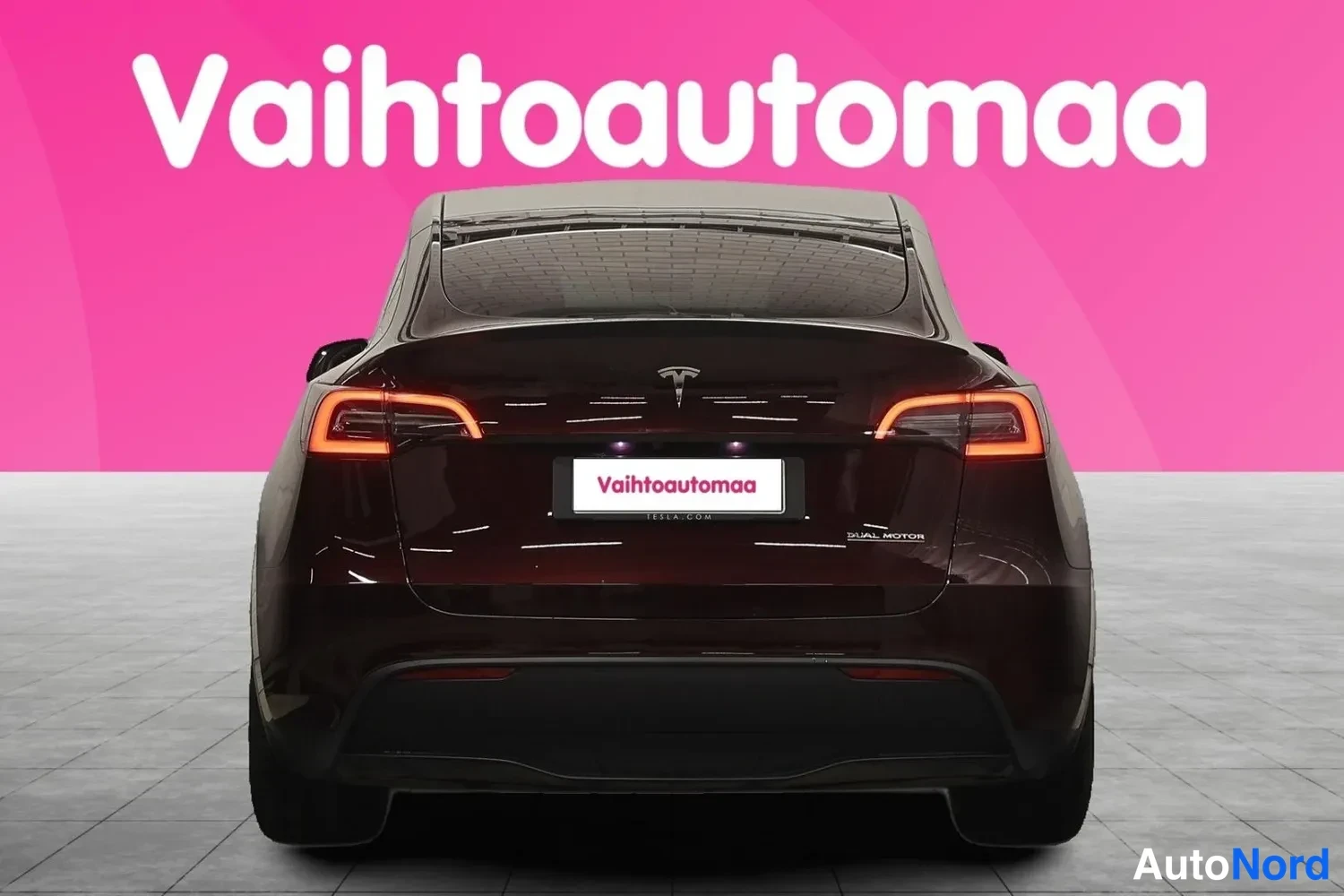 Takaa: Tesla Model Y suoraan takaa kuvattuna, takavalot päällä, konepellilla Tesla-tunnus ja takalokasuojassa DUAL MOTOR-teksti.