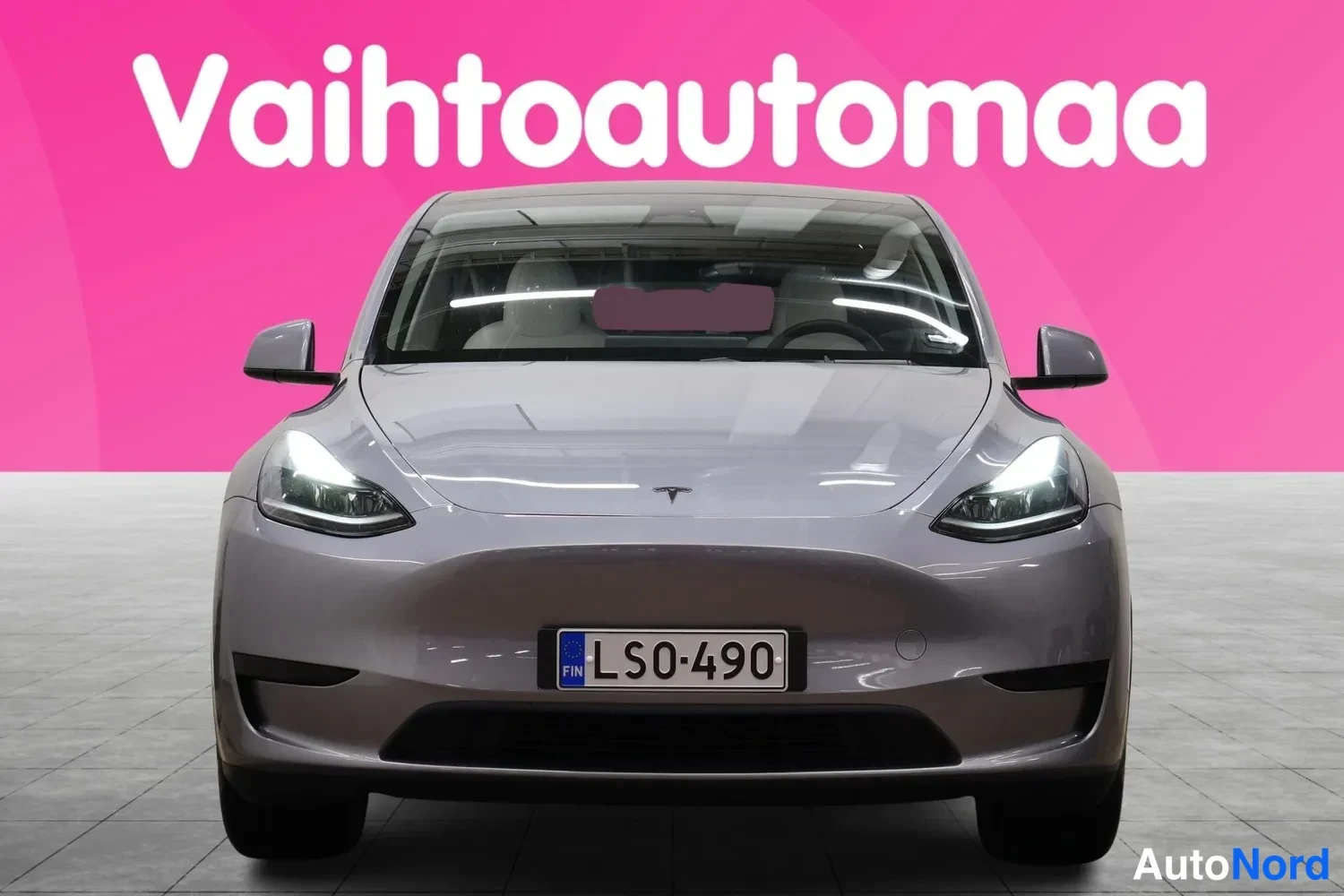 Edestä: Tesla Model Y -auto suoraan edestä kuvattuna, harmaanvärinen kori, rekisteritunnus etupuskurissa.