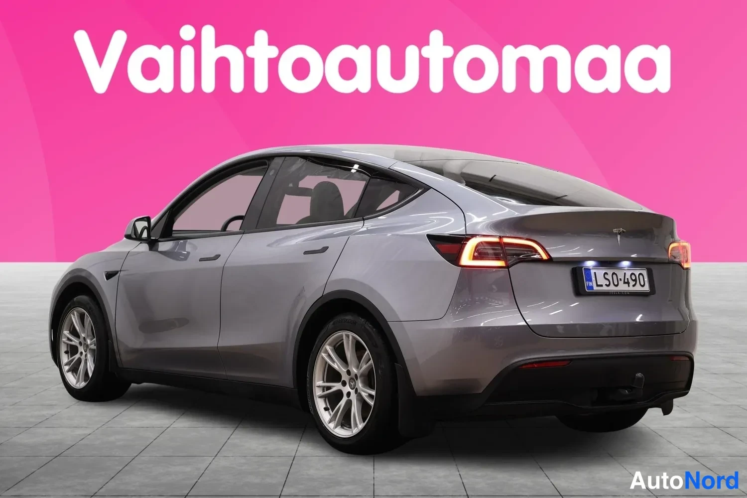 Takaviisto: Auton takaosan ja vasemman sivun kolmasosakuva vaaleanharmaa farmarimallinen auto, rekisterikilpi.