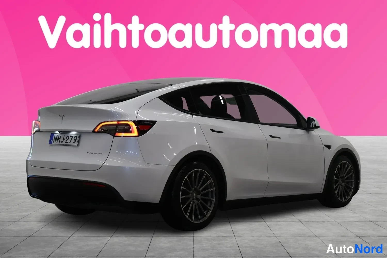 Takaviisto: Tesla Model Y -henkilöauton takaosa ja oikea kylki valkoisena sivulta-yläviistosta kuvattuna, rekisterikilpi.
