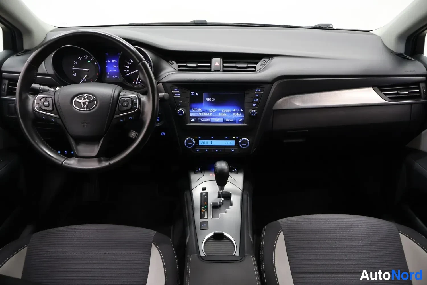 Muu: Ohjaamo suoraan edestä: Toyota-ohjauspyörä, mittaristo, keskinäyttö radiovalikoineen, automaattivaihteiston valitsin ja kaksi etuistuinta.