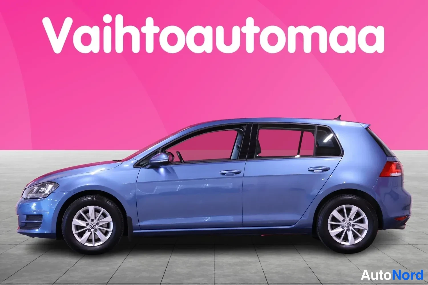 Etuviisto, nokka vasemmalle: Sininen Volkswagen Golf sivulta, keula hieman vasemmalle kääntyneenä, vaaleanpunaisella taustalla.