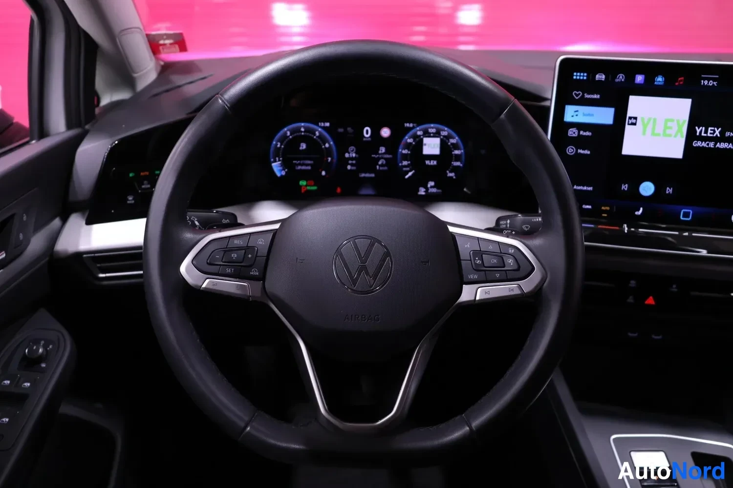 Muu: Sisäkuva auton ohjaamosta: musta Volkswagen-ohjauspyörä AIRBAG-tekstillä ja mallimerkeillä, digitaalinen mittaristo näyttää nopeuden 0, ja keskellä oleva infota