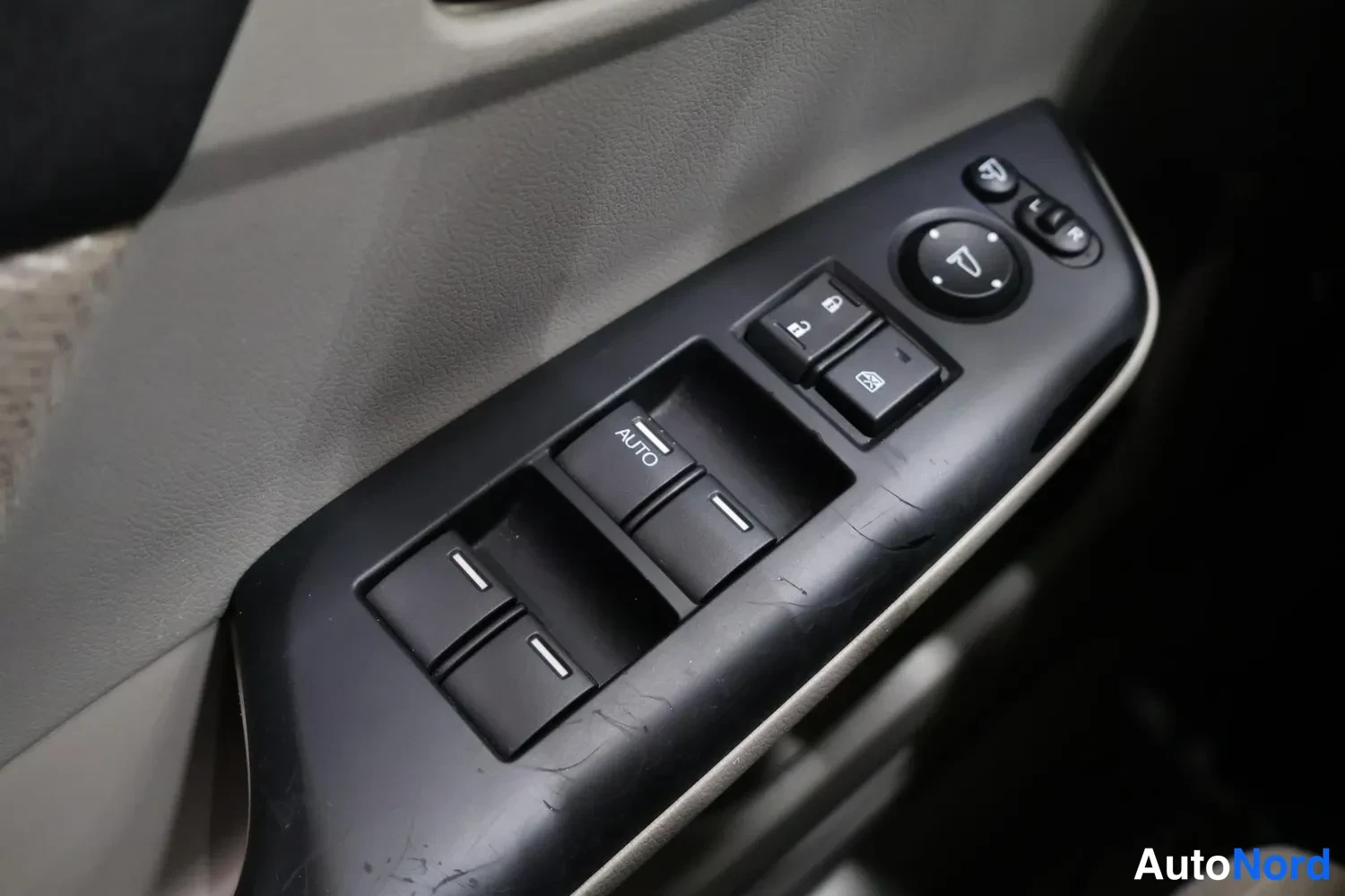 Sivulta: Oven sisäpaneelin kytkinryhmä lähikuvassa: ikkunannostinkytkimiä, joista yhdessä AUTO-teksti, keskellä peilien säätöruuvi ja peilien taittokytkin sekä ovien luk