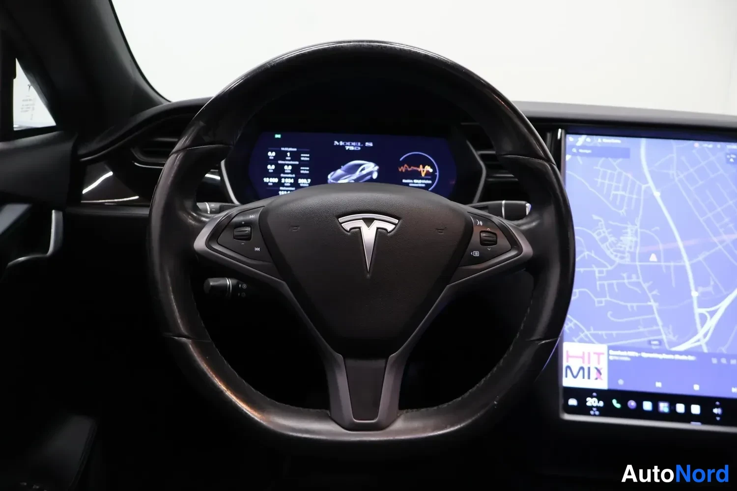 Muu: Tesla Model S:än ohjaamo: musta ohjauspyörä Teslan logolla, kuljettajan edessä digitaalinen mittaristonäyttö ja oikealla suuri keskinäinen kosketusnäyttö, jossa