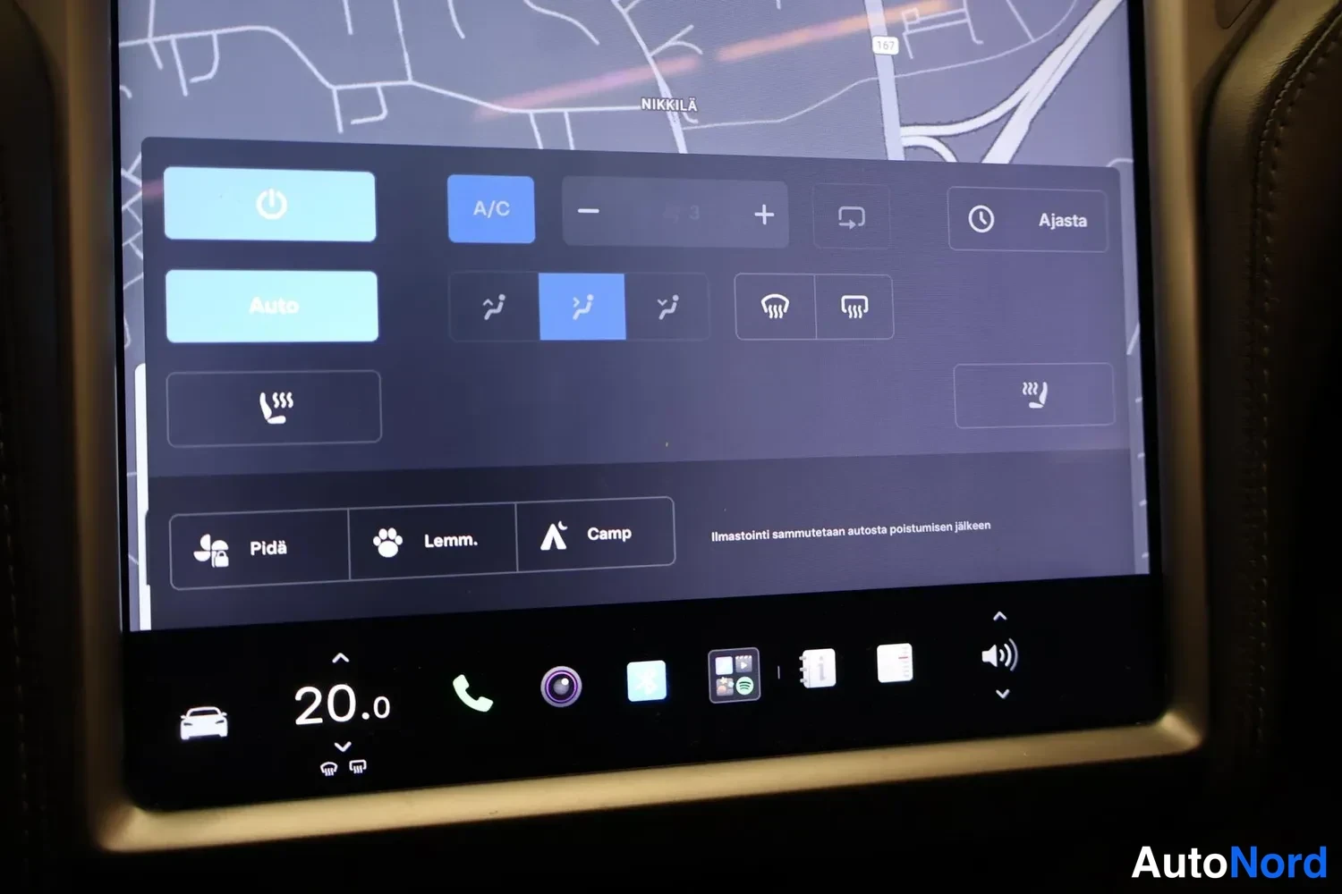 Muu: Kohtakuva auton infotainment-näytöstä: ilmastointivalikko näkyvissä A/C-painikkeella, istuinlämmityskuvakkeilla ja kartta taustalla.