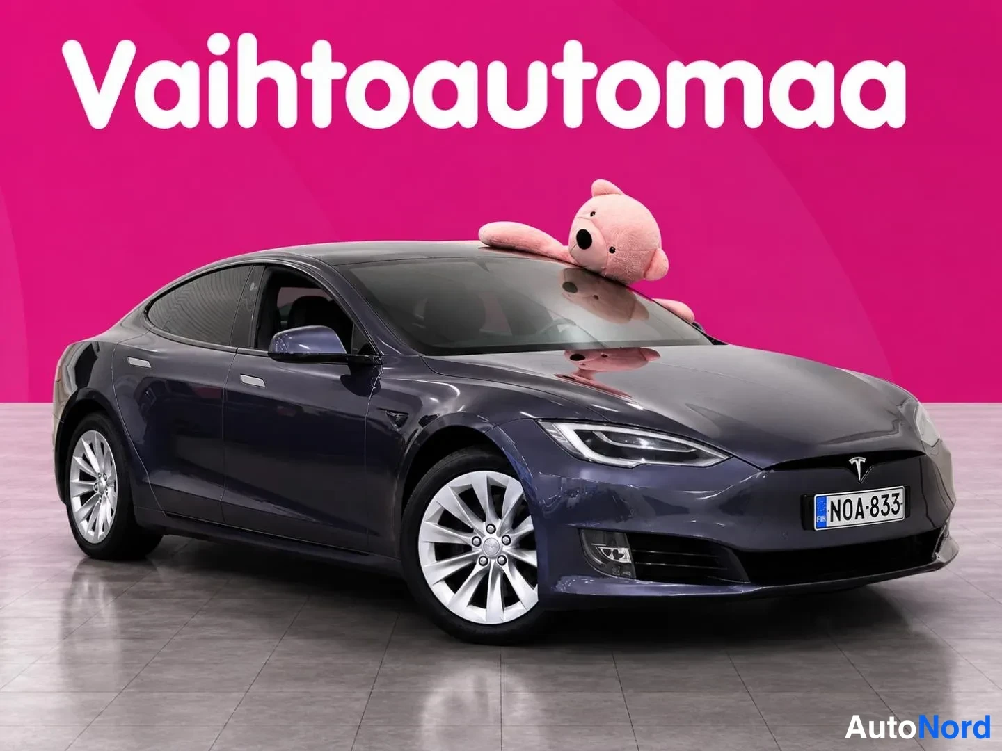 Etuviisto, nokka oikealle: Tummansininen Tesla Model S -sedan etuokolikuva oikealta, rekisteritunnus, valkorengaskoristeet.